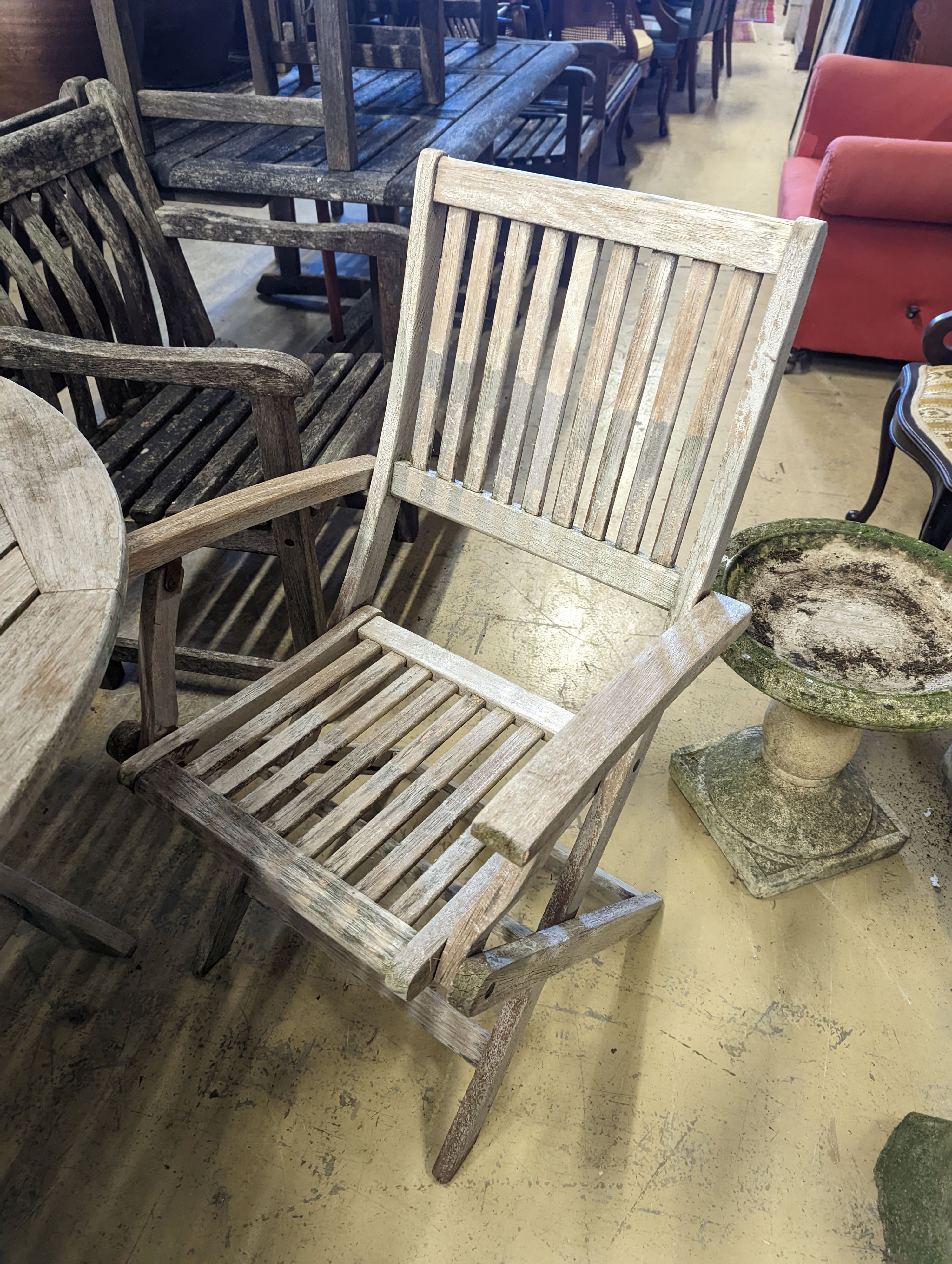 A circular weathered teak folding garden table, diameter 120cm, height 74cm, four folding elbow chairs and a parasol